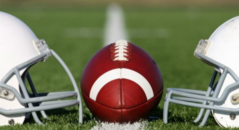 Two football helmets and a football on sitting on a football field